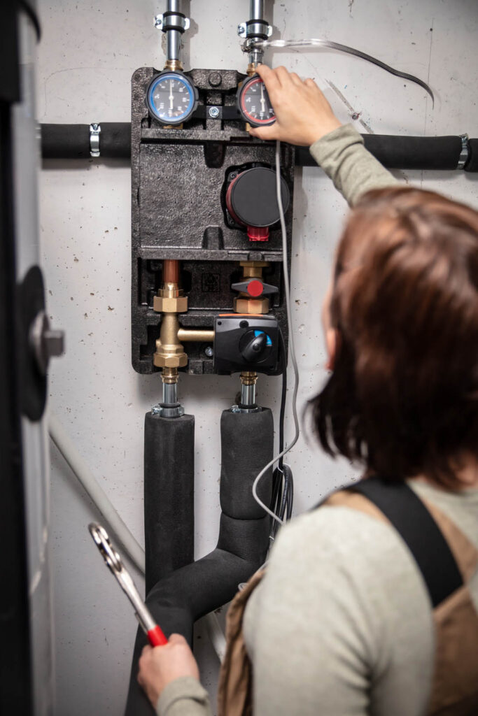 female plumber with pipe wrench installs parts of a pellet heating system in the basement